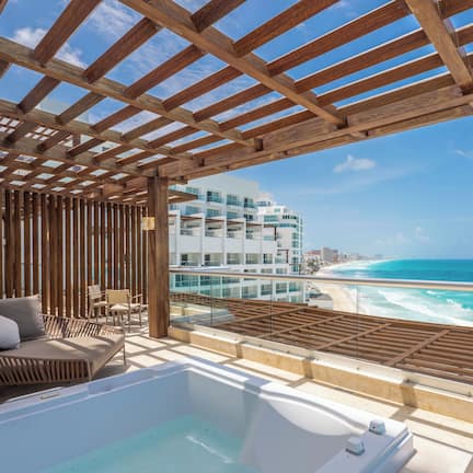 A balcony with a wooden pergola, a hot tub, and a view of the beach and ocean.