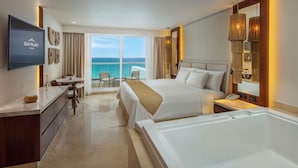 A hotel room with a large bed, a separate sofa, a dining area, and a view of the ocean. - Sun Palace Cancun - Adults Only - All-inclusive (Cancun)