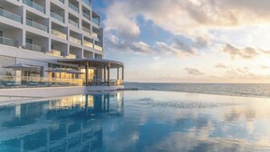 A modern hotel with a pool, a covered area with seating, and a view of the sea. - Sun Palace Cancun - Adults Only - All-inclusive (Cancun)