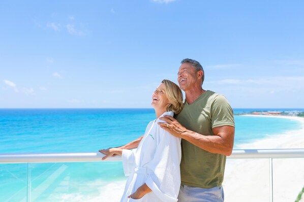 Una pareja en un balcón con vista a una playa bajo cielos despejados.