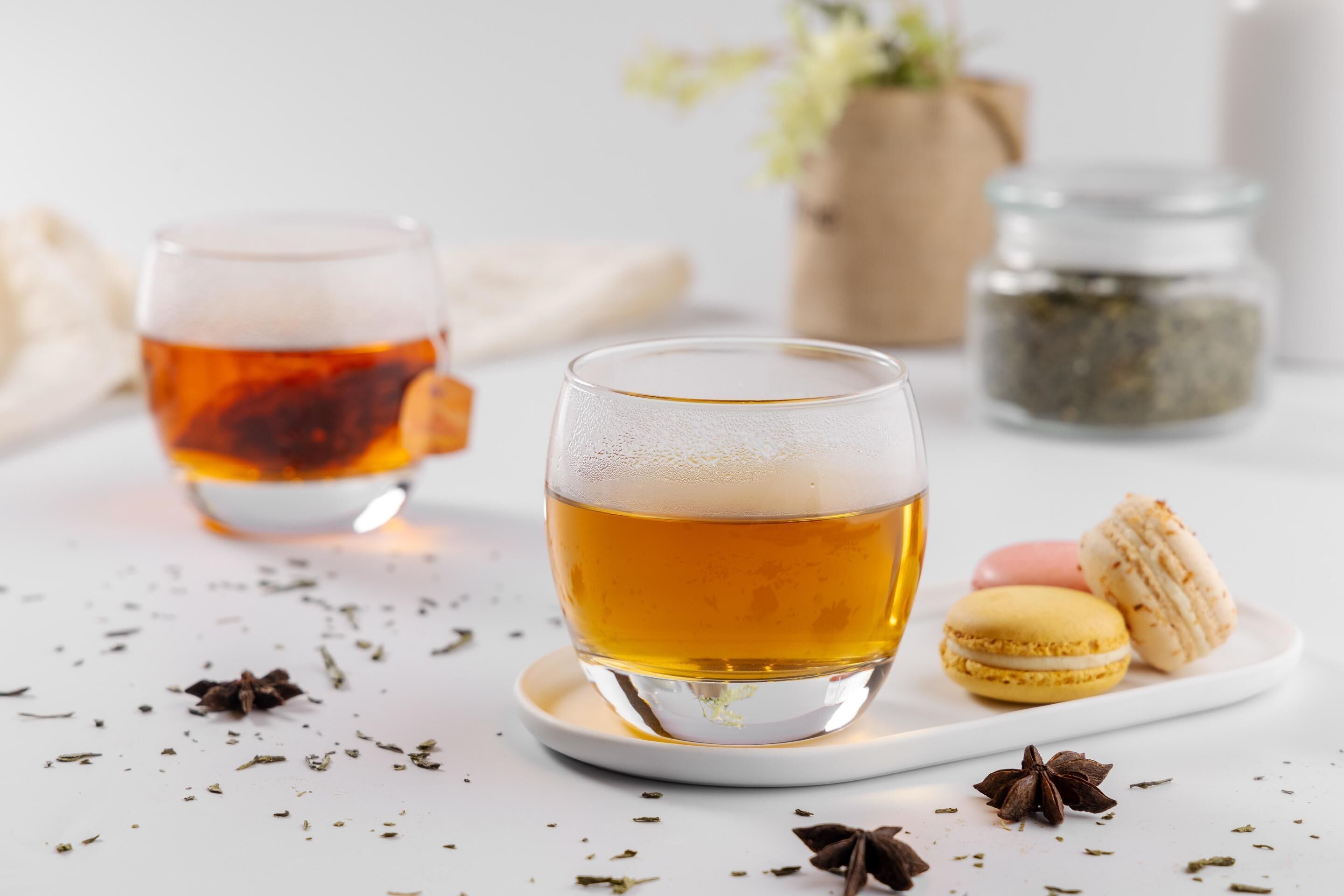 A glass of amber liquid on a white coaster, a plate with macarons, and scattered spices.