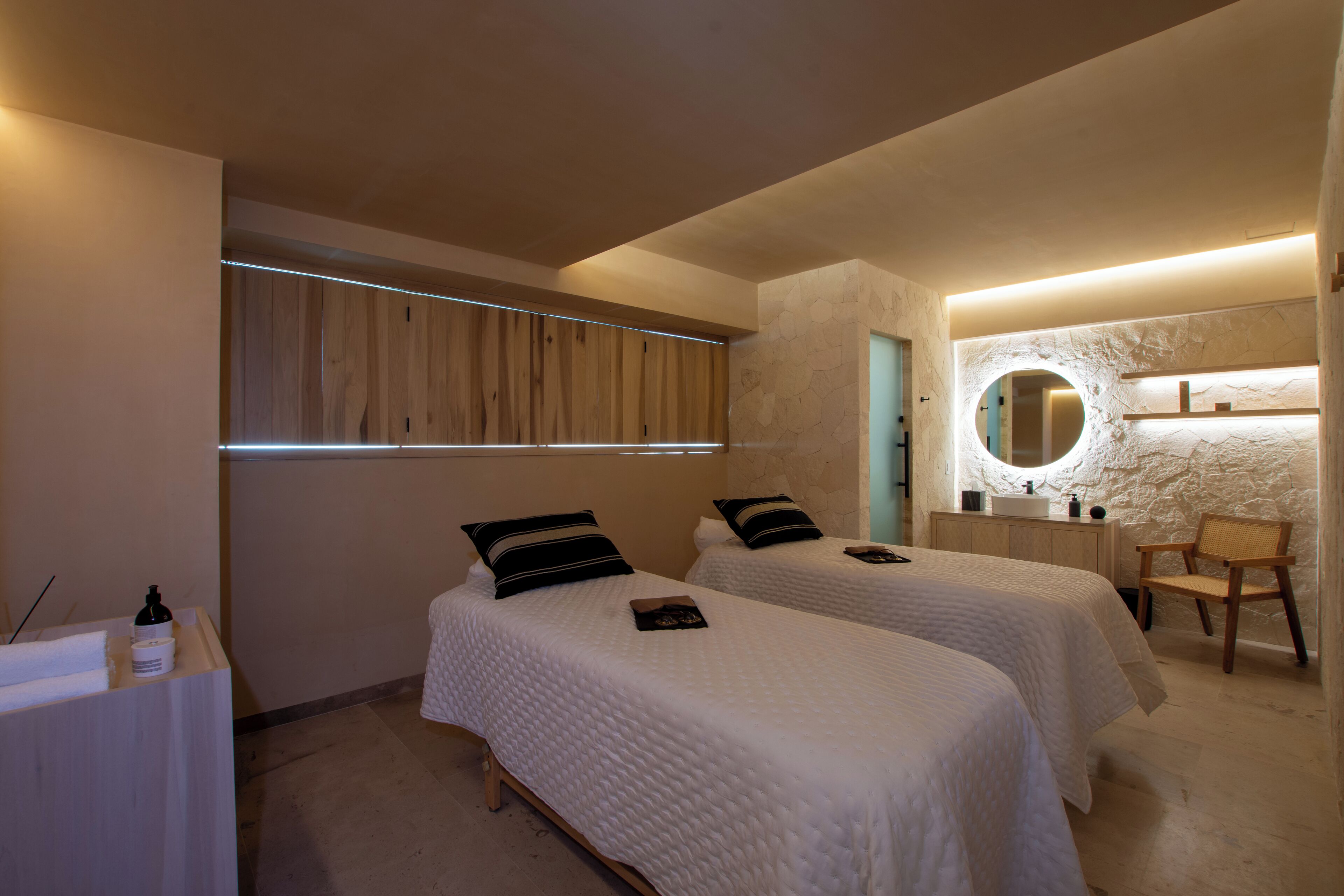 Un dormitorio con dos camas, un armario de madera, un espejo redondo y una pequeña zona de estar.