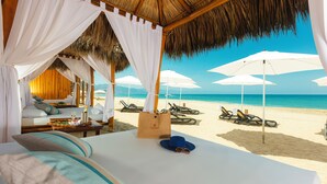 Una habitación frente a la playa con cama, cortinas blancas y vistas al mar.