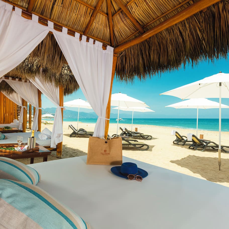 A beachside room with a bed, white curtains, and a view of the beach and ocean.