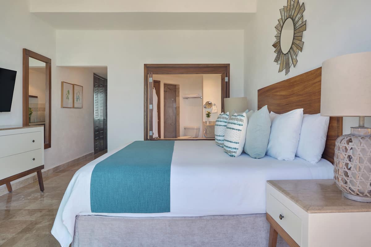 A bedroom with a bed, bedside table, lamp, and a mirror on the wall.