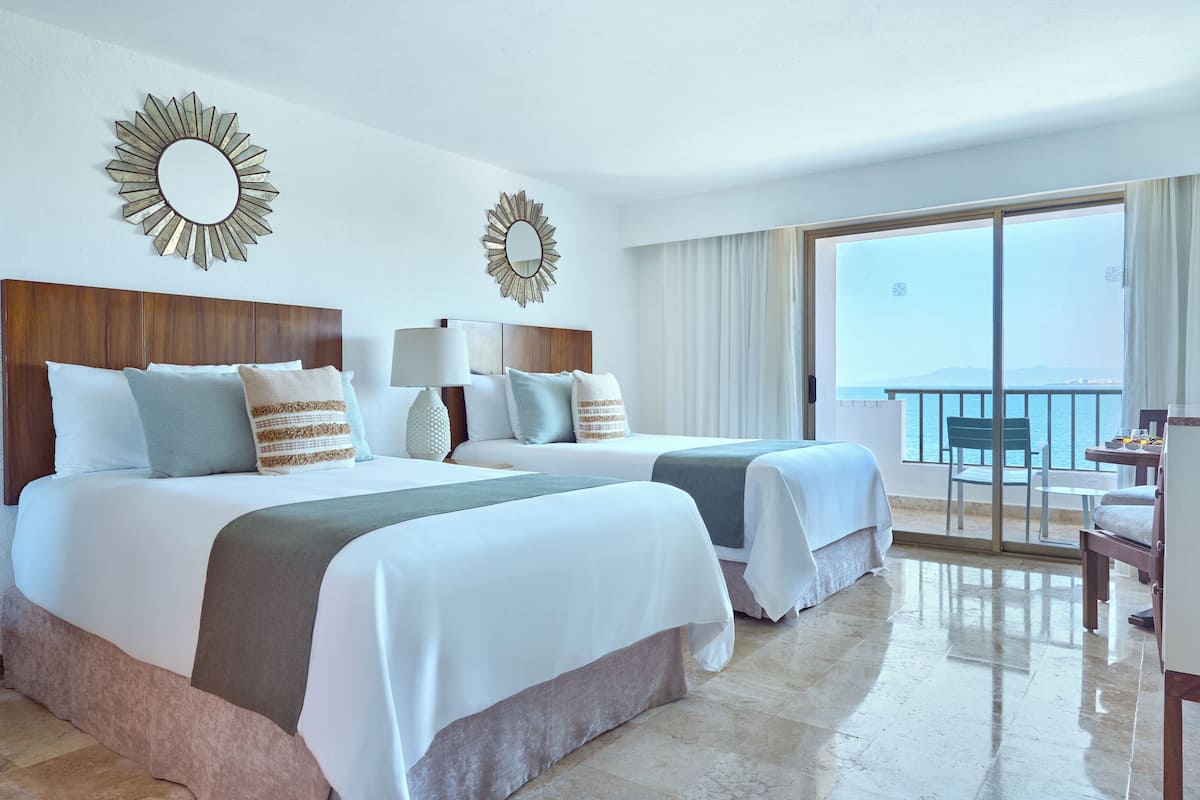 A hotel room with two beds, a balcony with a view, and a dining area.