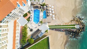 Vista aérea de un resort con piscina, zona de playa y costa rocosa.