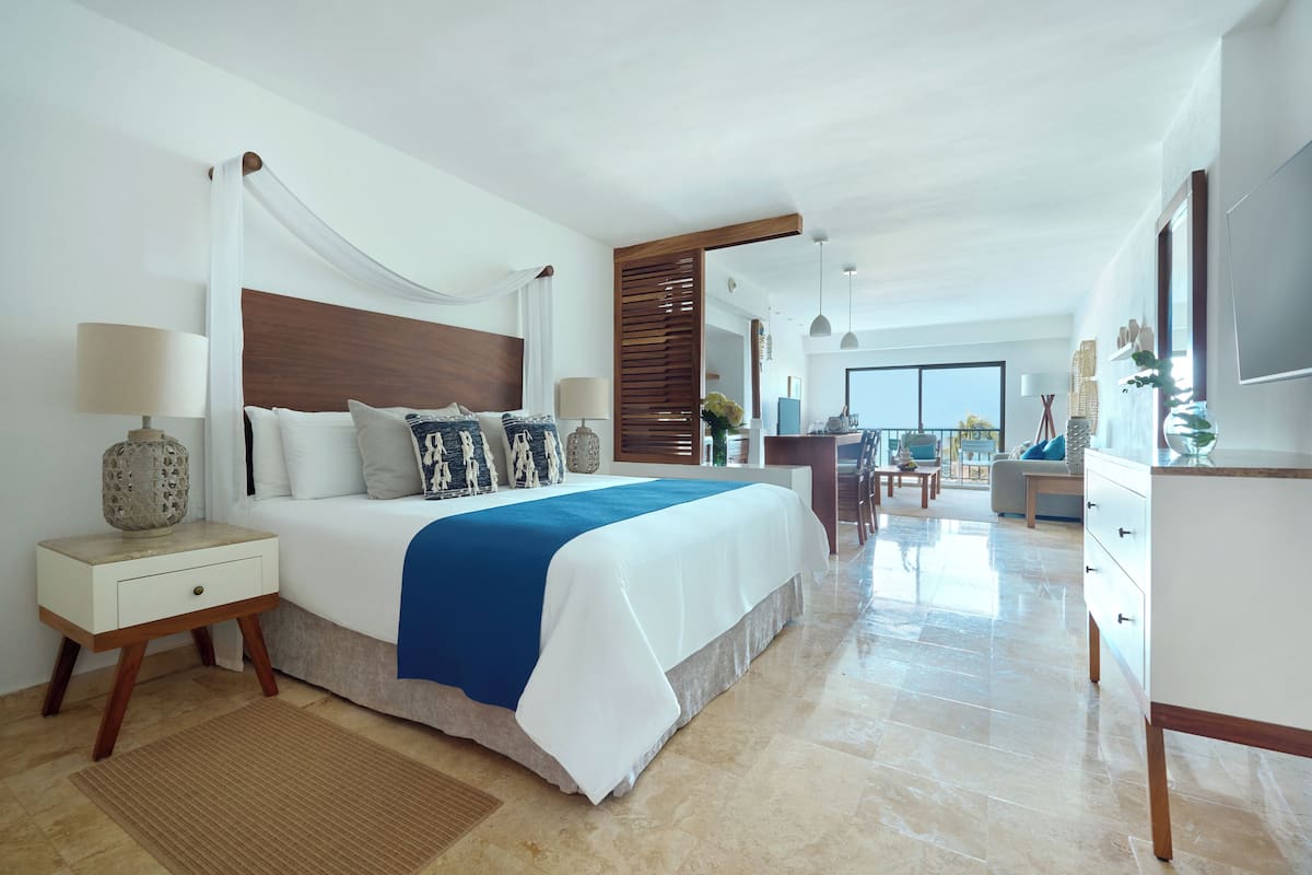 A spacious bedroom with a large bed, bedside tables, a desk, and a view of the balcony.