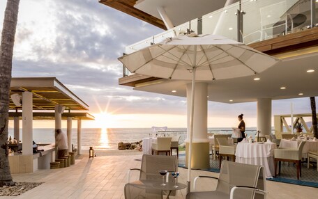 An outdoor seating area with tables and chairs, overlooking the ocean.