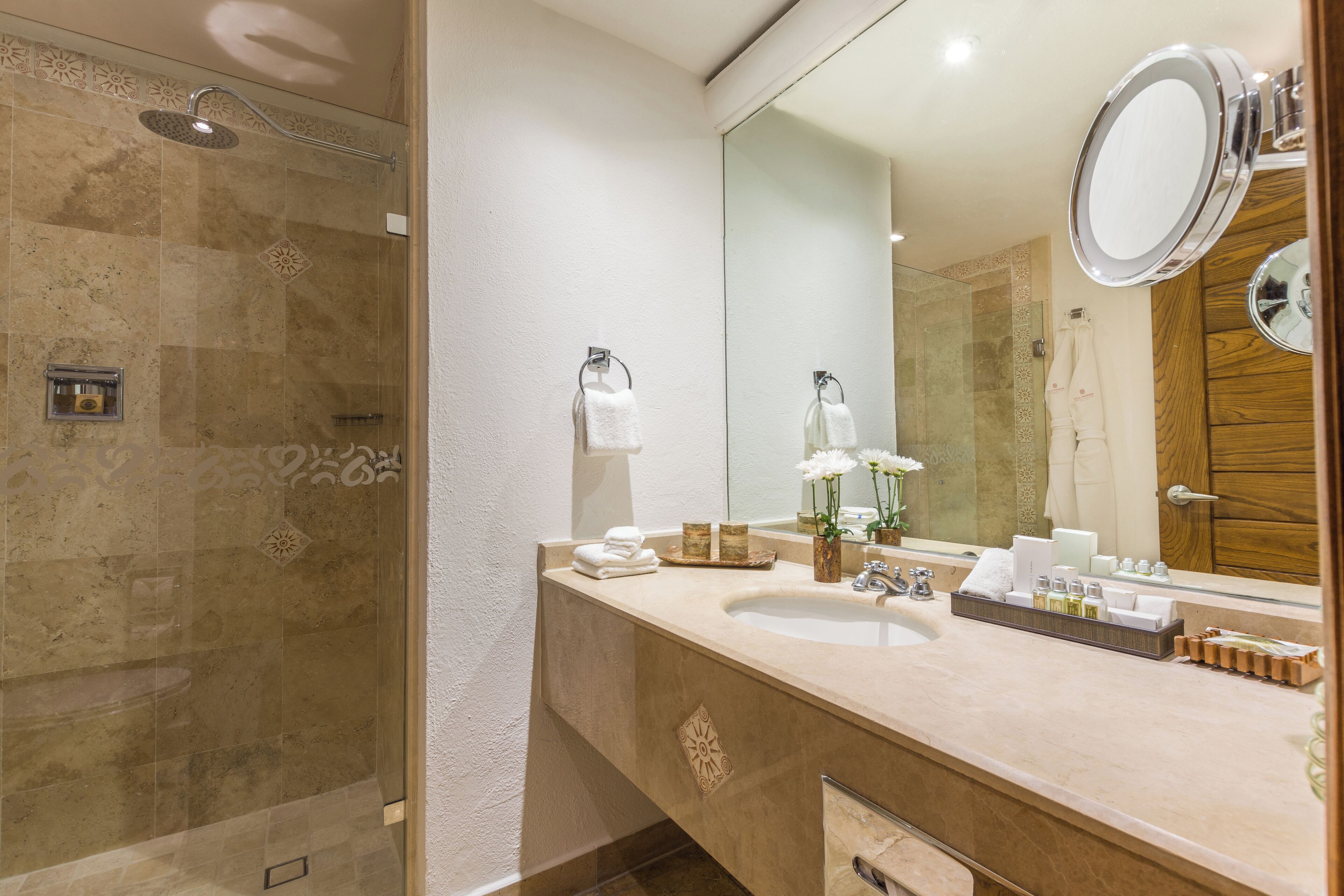 A modern bathroom with a glass-enclosed shower, a large mirror, and a vanity with toiletries.