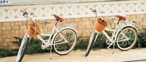 Two white bicycles with baskets and brown seats parked on a tiled surface.