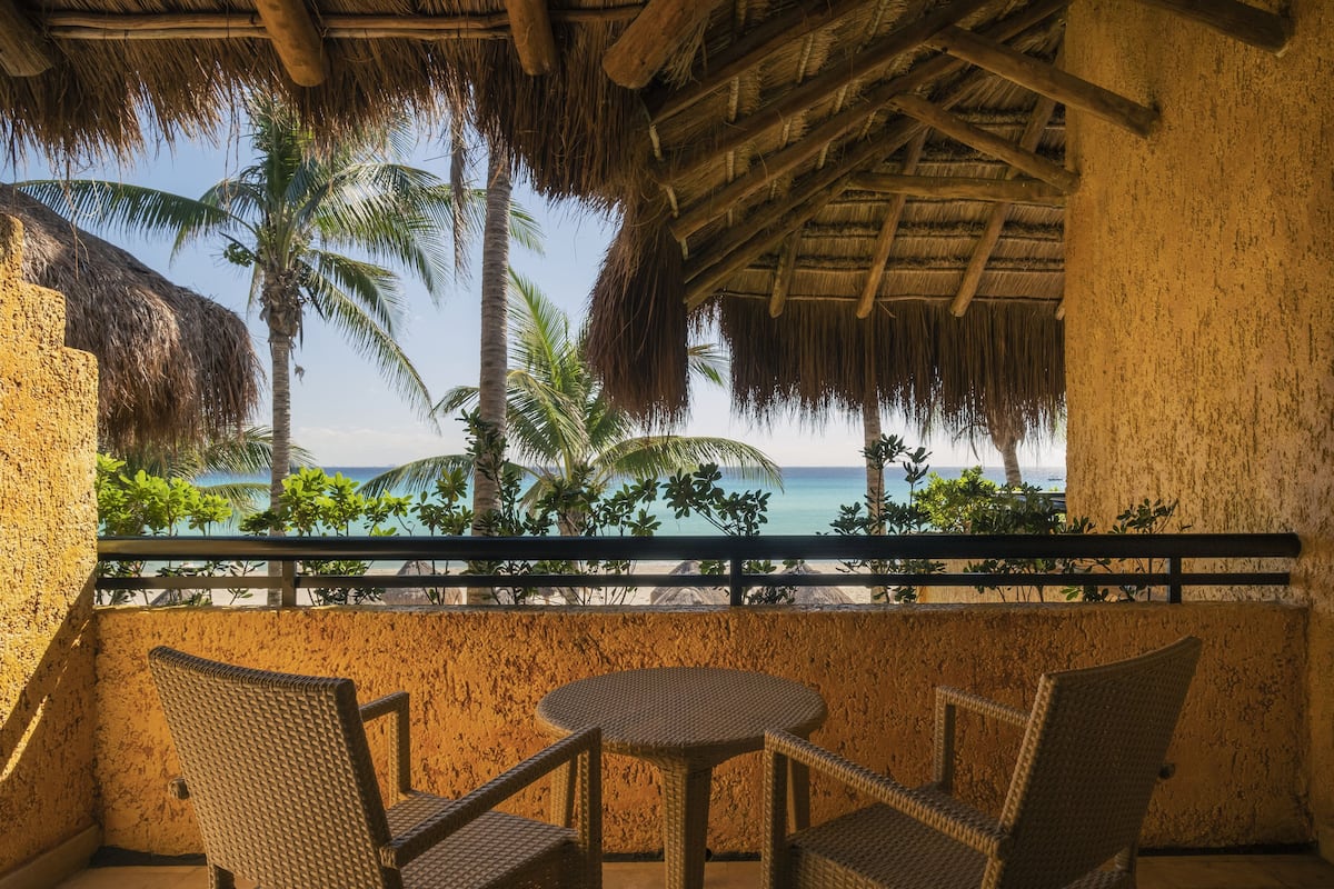 Een balkon met rieten meubels en uitzicht op het strand en palmbomen.