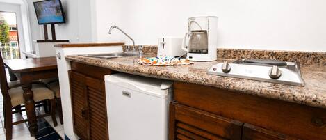 A compact kitchen with a built-in dishwasher, a coffee maker, and a TV mounted on the wall.