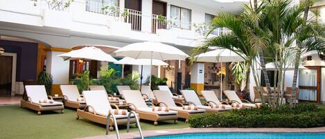 A hotel pool area with lounge chairs, umbrellas, and a clear blue pool.