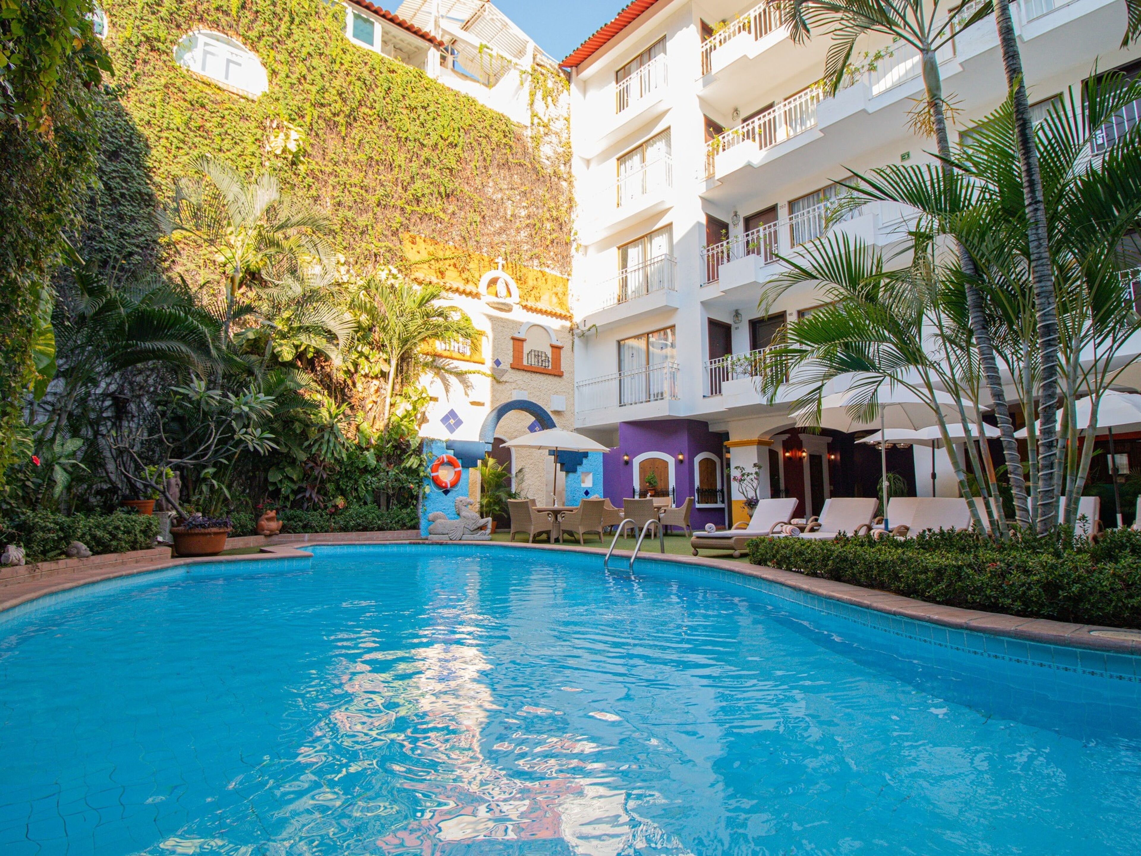 Una piscina rodeada de abundante vegetación y un edificio de varios pisos con balcones.