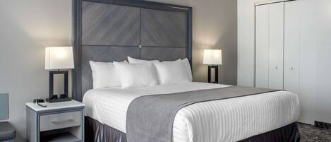 A hotel room with a large bed, two bedside tables with lamps, a nightstand, a chair, and a wardrobe.
