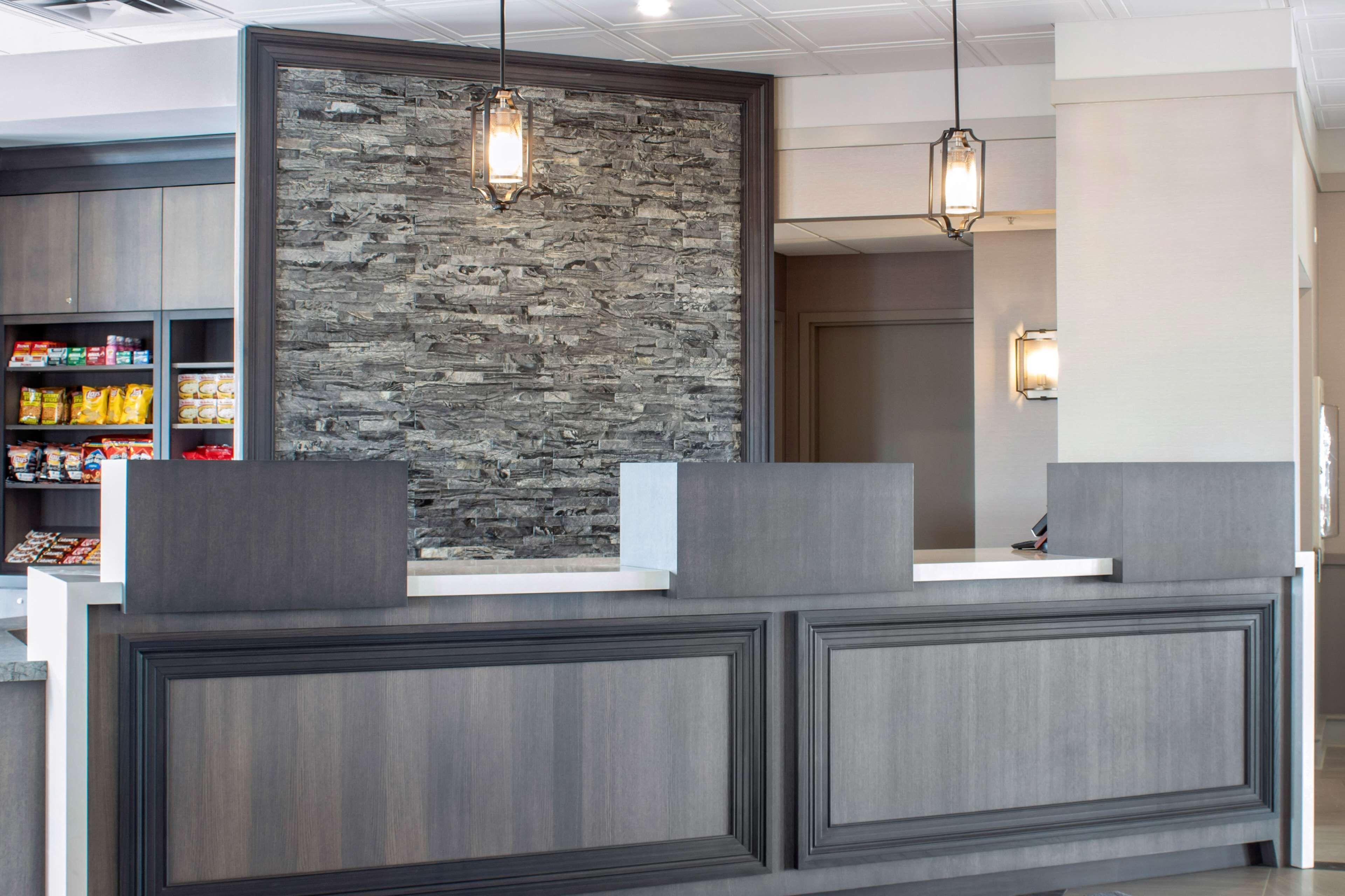 A reception desk with a stone wall backdrop, pendant lighting, and a shelf with snacks.