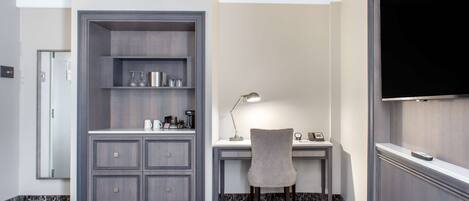 A modern hotel room with a built-in desk, a chair, a television, and a minibar.