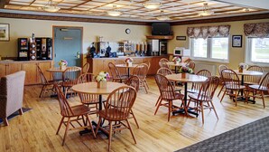 Un restaurant avec des tables et des chaises en bois, un coin bar et un téléviseur placé au-dessus du bar.
