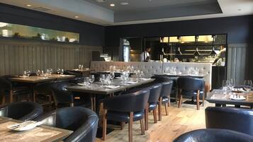 Un restaurante con mesas preparadas para comer, una zona de bar y vistas a la ciudad.