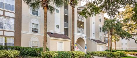 A multi-story residential building with a central courtyard, palm trees, and a well-maintained lawn.