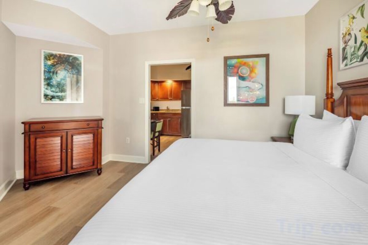 A hotel room with a large bed, a wooden dresser, and artwork on the walls.