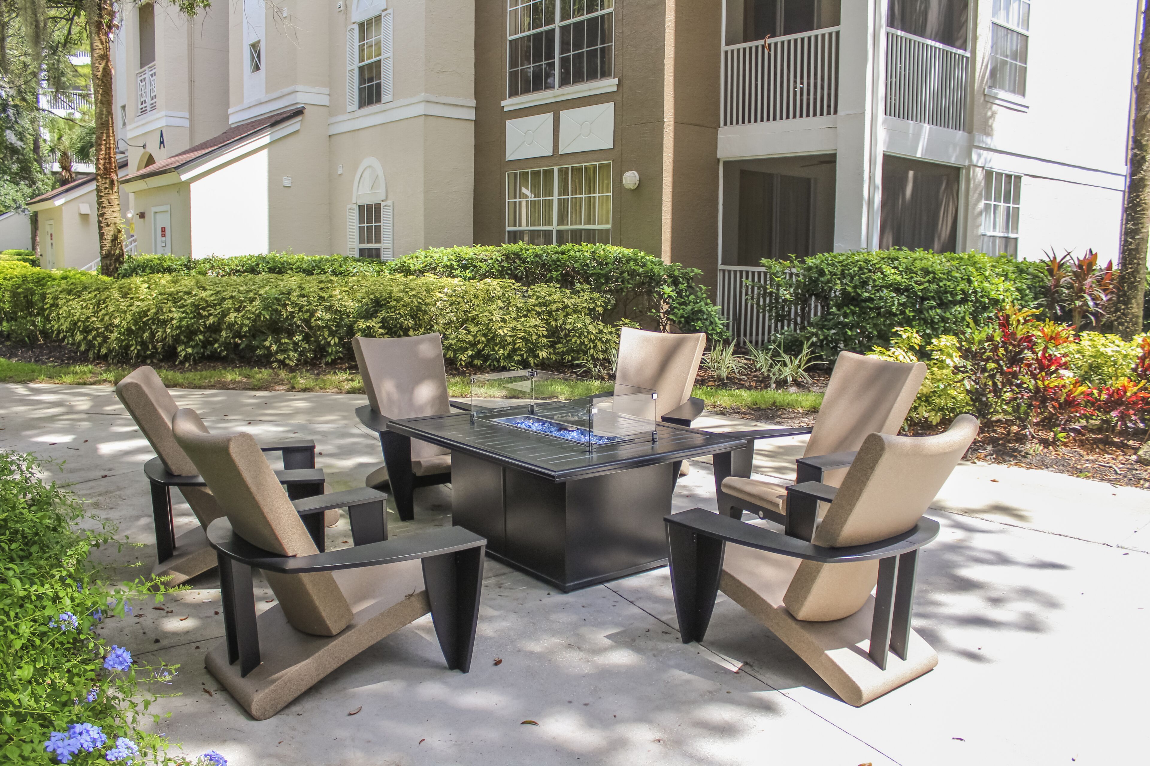 Un espace extérieur aménagé avec une table rectangulaire et quatre chaises, entouré de haies bien entretenues et avec un bâtiment en arrière-plan.