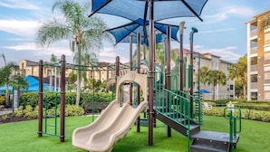 A playground with a slide, climbing structures, and a shaded area.