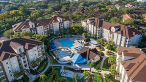 Un complejo residencial con varios edificios de apartamentos, un área de piscina central con sillones de descanso y jardines bien cuidados.