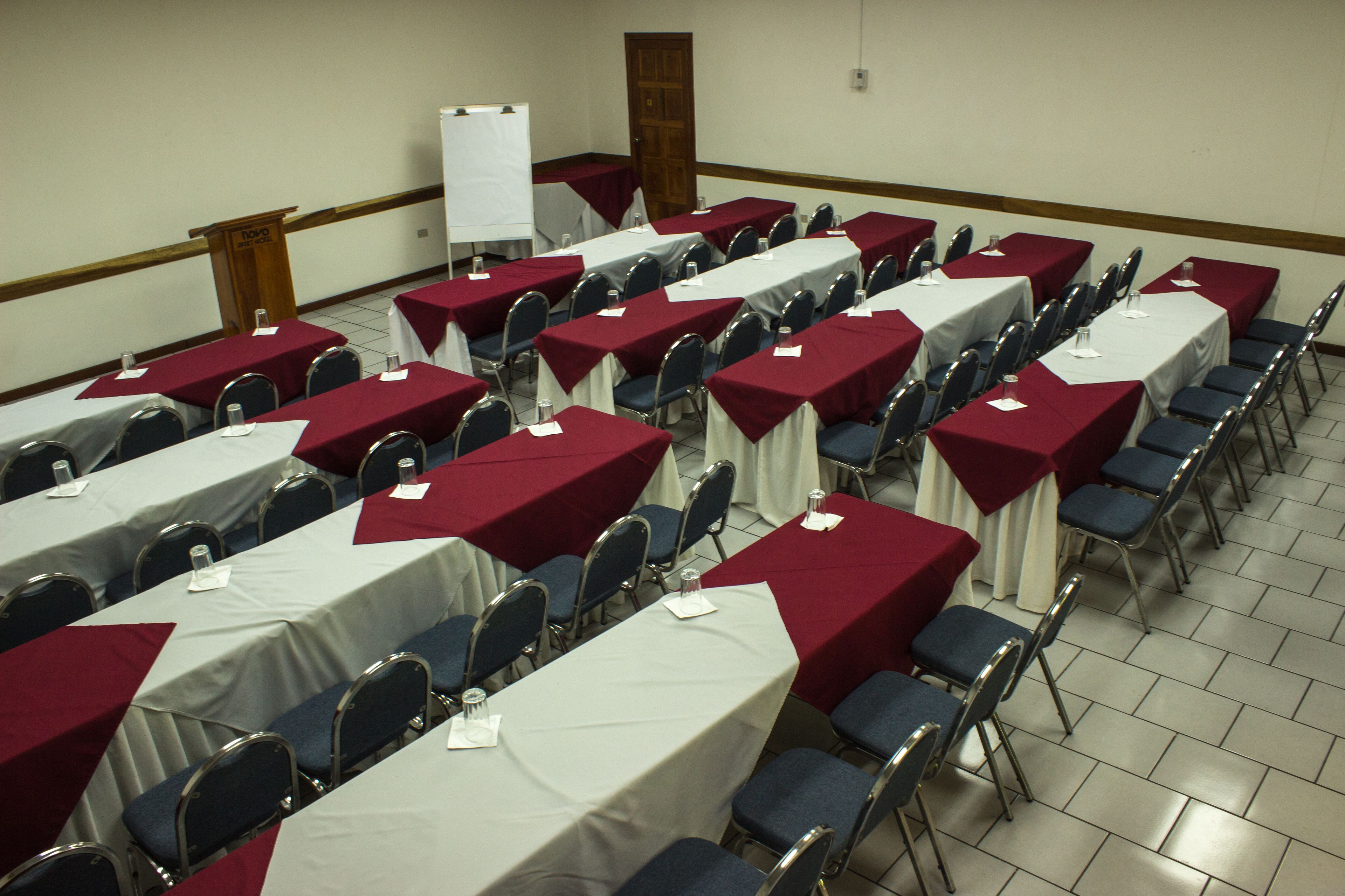 Un salón de conferencias con filas de mesas y sillas, una pizarra y un atril.