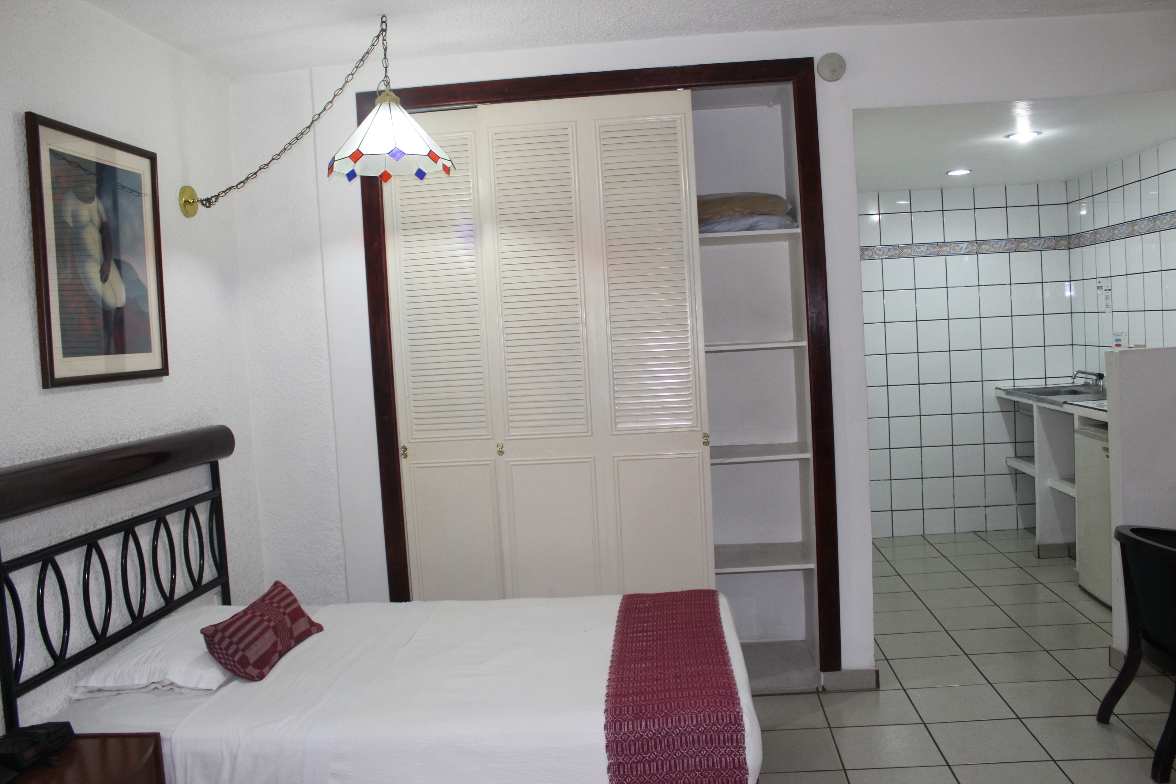 Un dormitorio con cama, armario y baño visible a través de una puerta abierta.