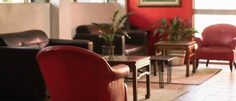 A living room with a red armchair, a brown leather sofa, and a wooden coffee table. There are potted plants on a side table and a painting on the wall.
