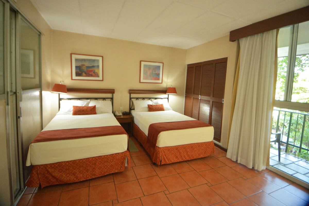 Habitación de hotel con dos camas, un balcón y una ventana con cortinas.