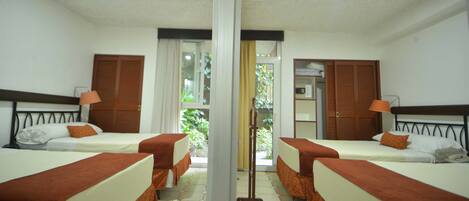 A hotel room with two beds, a mirror, a door, and a view of greenery outside.