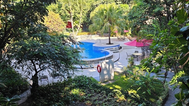 Ein Poolbereich mit einem kreisförmigen Wasserspiel, umgeben von üppiger Bepflanzung und Sitzgelegenheiten im Freien.