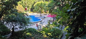 Un área de piscina con una fuente de agua circular, rodeada de exuberante vegetación y mobiliario de exterior.