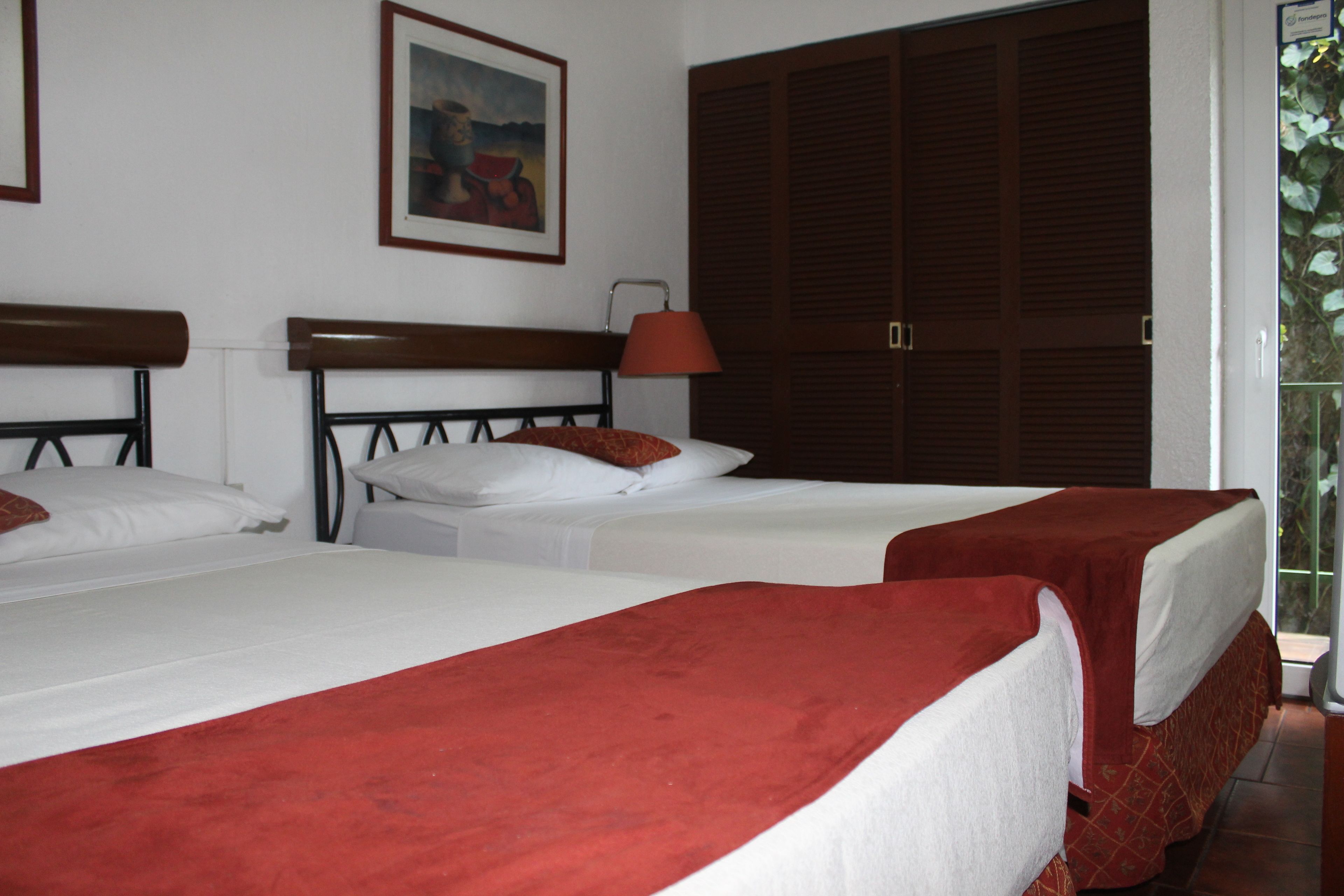 Habitación de hotel con dos camas, un armario grande, un cuadro en la pared y una ventana con vistas.