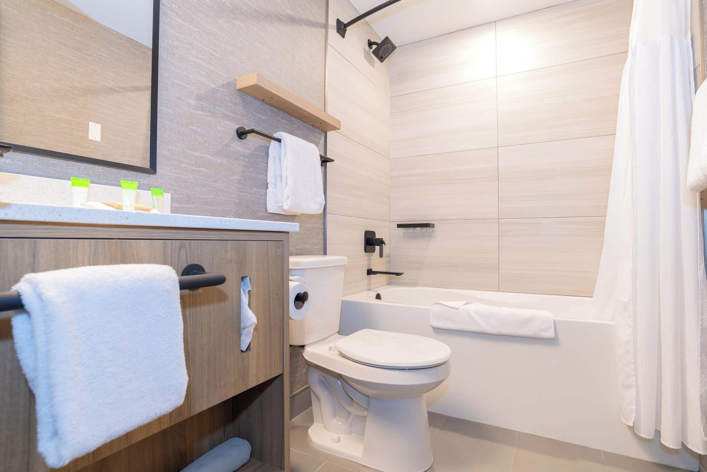 A modern bathroom with a toilet, bathtub, and a wooden vanity with a towel rack.