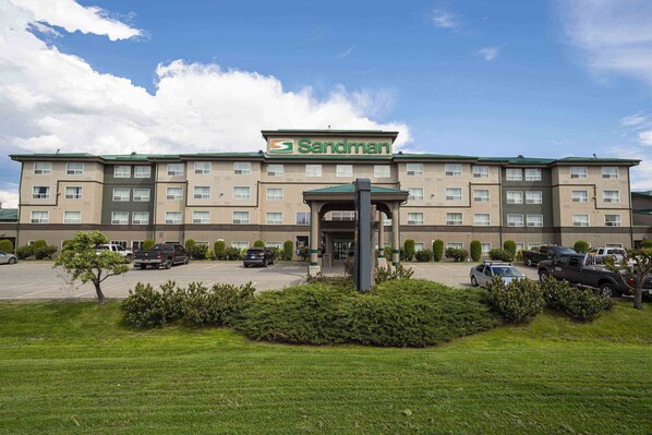 Een Sandman hotel met een centrale ingang, meerdere verdiepingen en een parkeerplaats.
