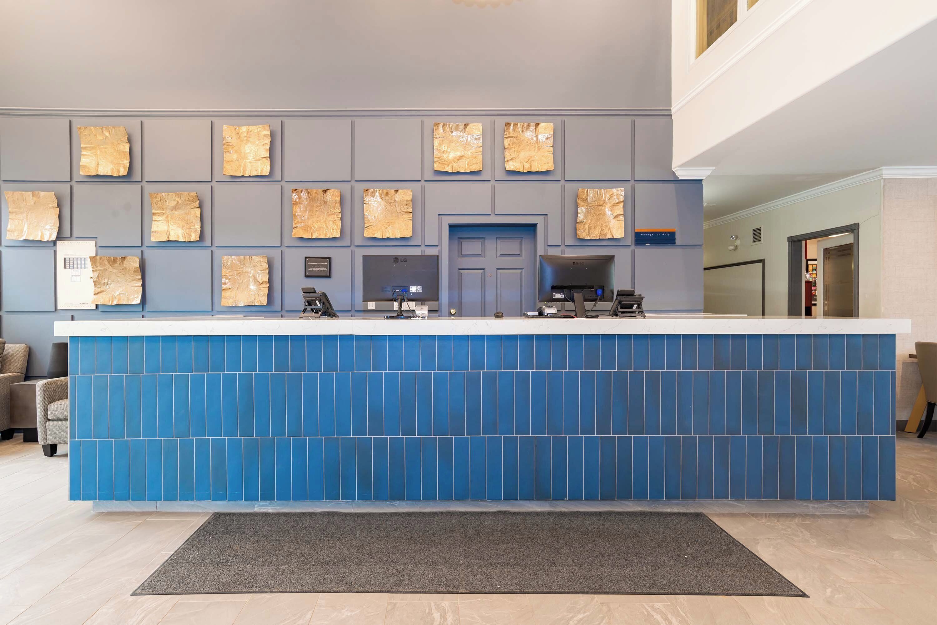 A reception desk with a blue tiled front, a gray wall with framed artwork, and a door in the center.