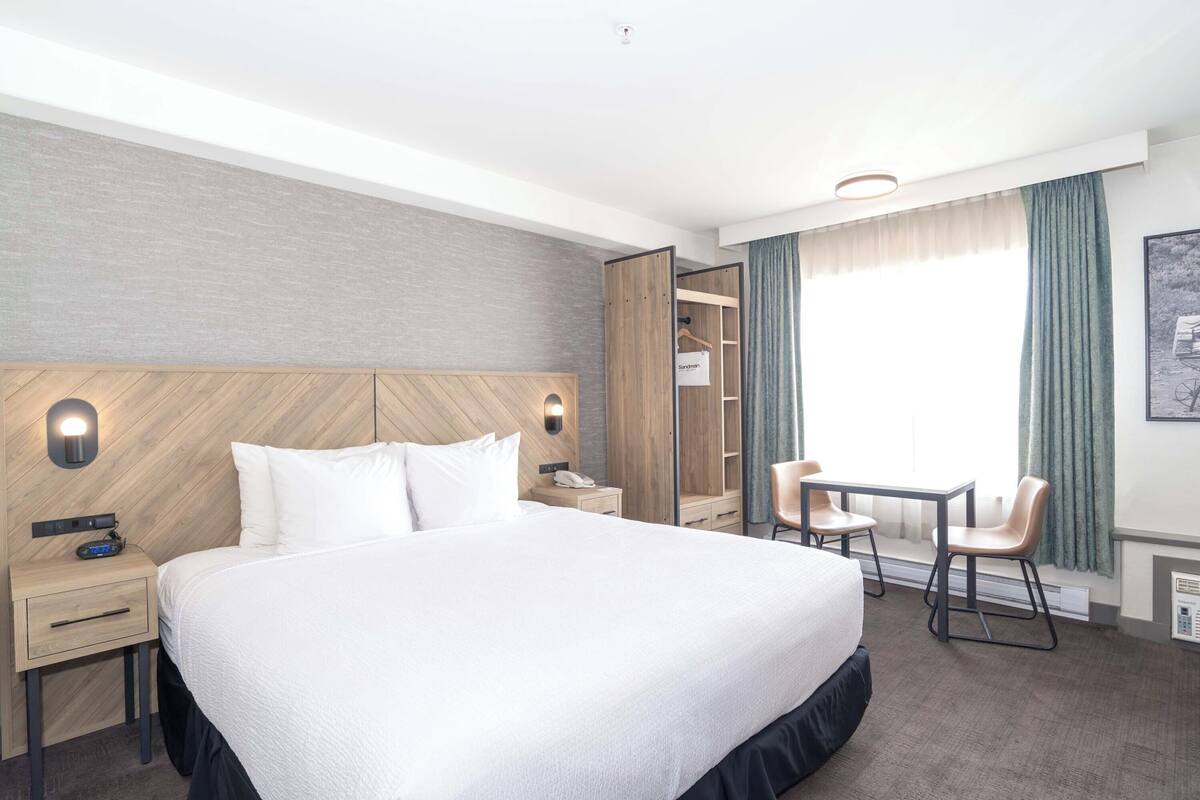 A hotel room with a large bed, a desk with two chairs, a wardrobe, and a window with curtains.