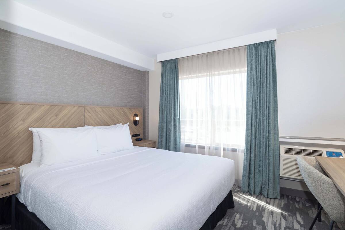 A hotel room with a large bed, a desk, and a window with curtains.