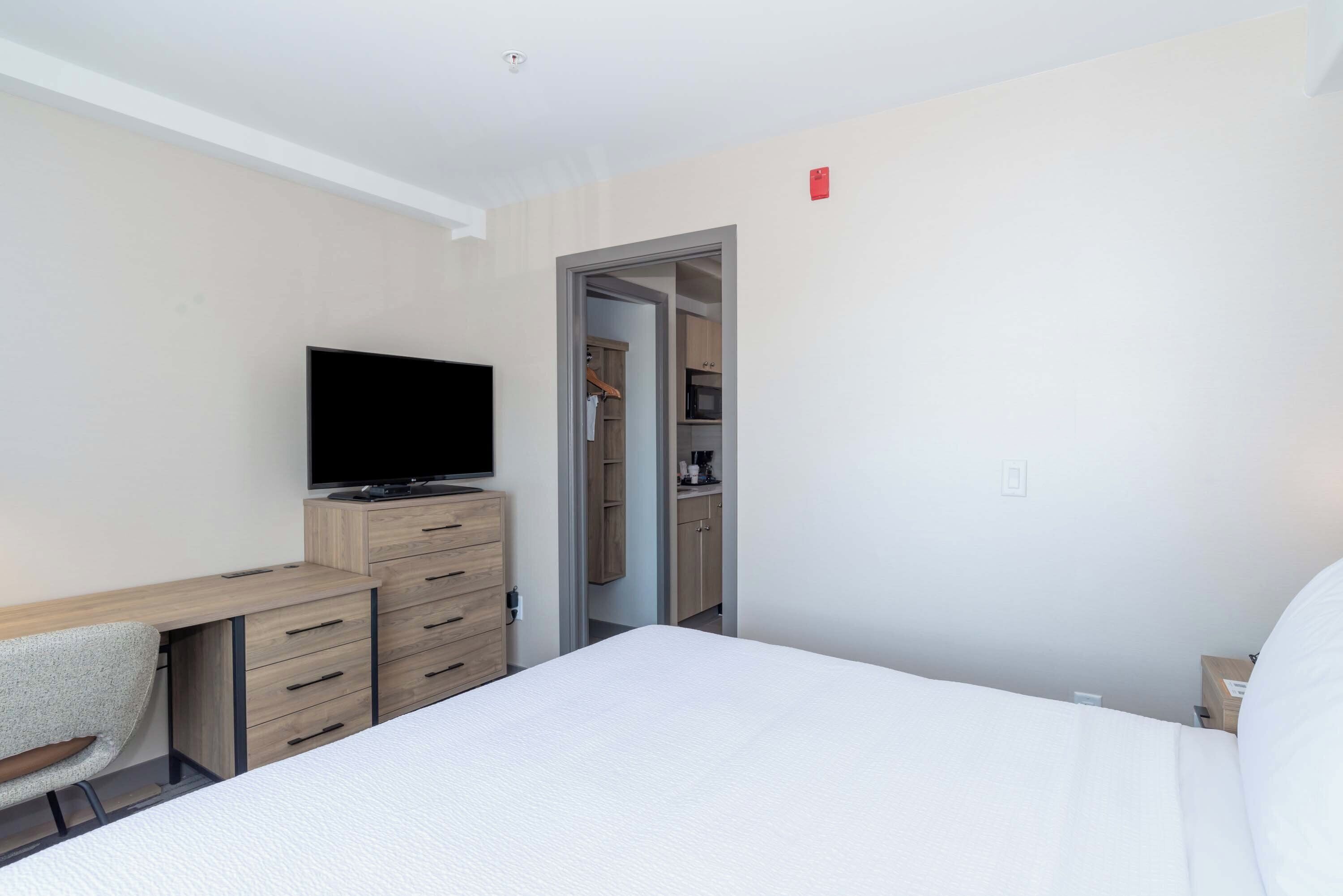 Een hotelkamer met een bed, een bureau met een televisie, een stoel en een kledingkast.
