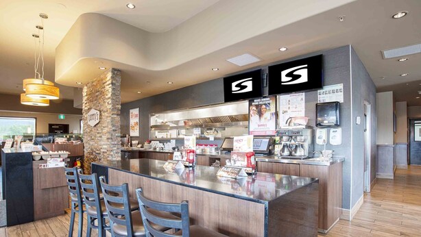 A modern bar area with a stone pillar, a counter with a logo, and a seating area with chairs. - Sandman Hotel Quesnel (Quesnel)