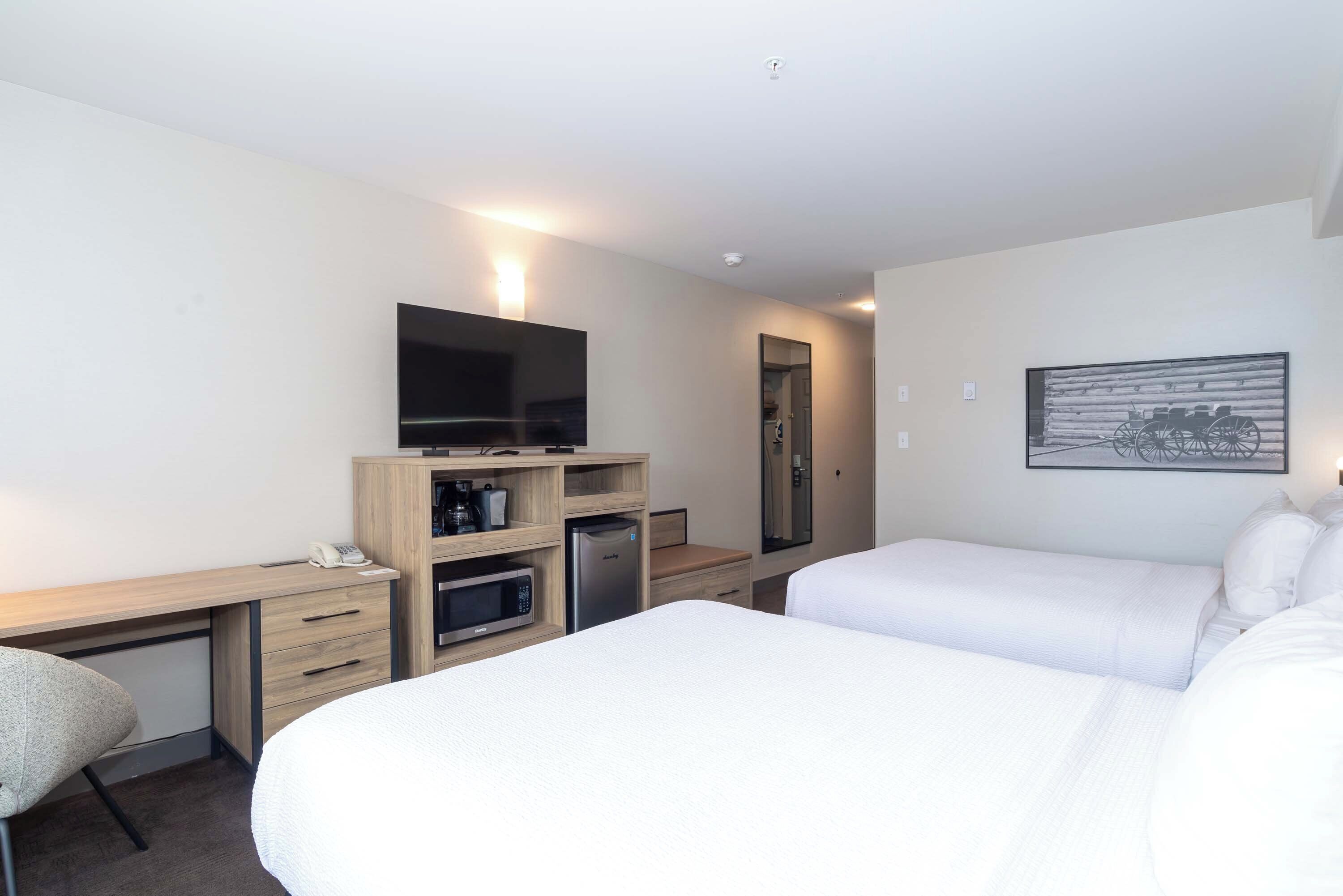 A hotel room with a bed, a desk with a flat-screen TV, a microwave, and a refrigerator.