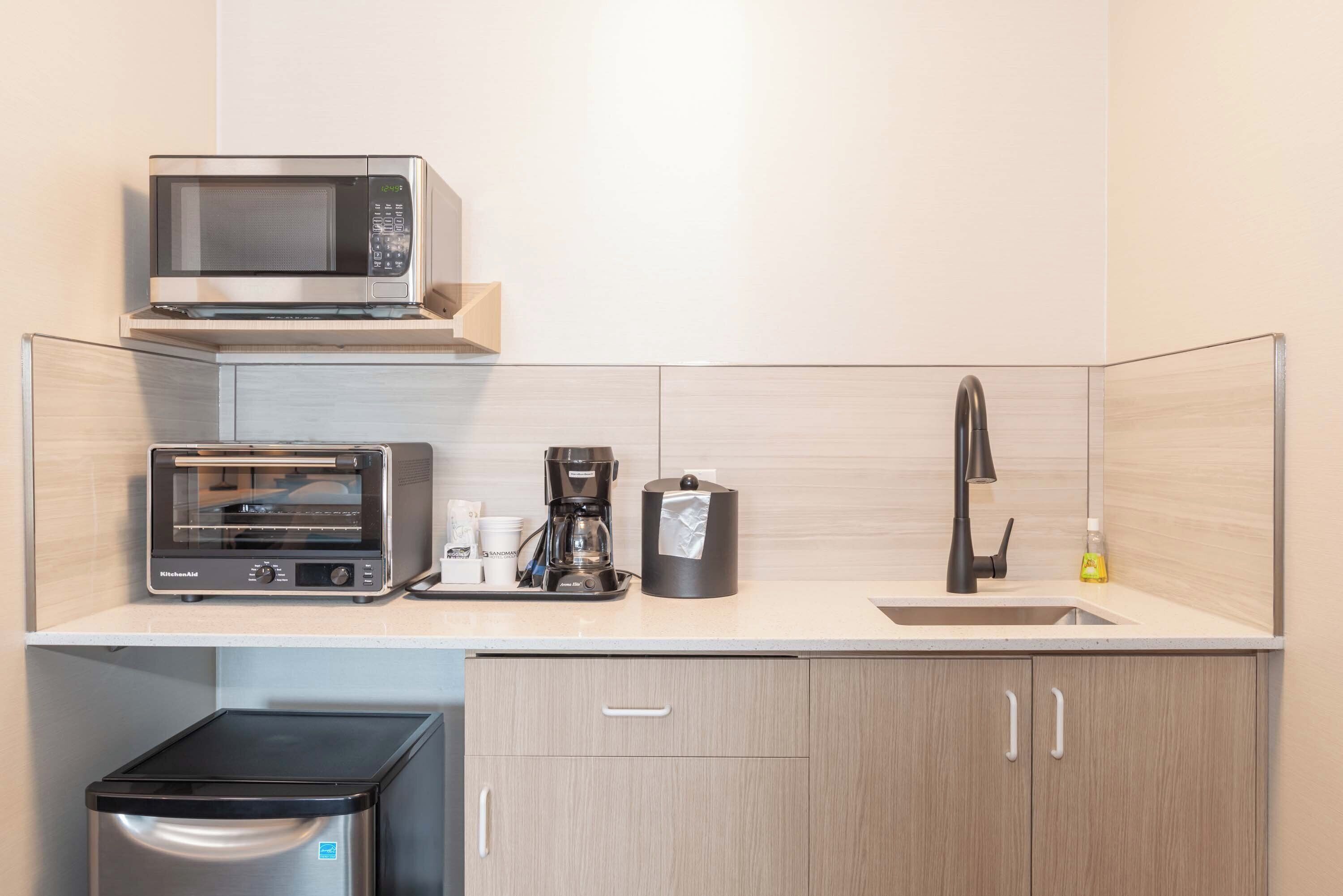 A compact kitchen with a microwave, toaster oven, coffee maker, and a sink.