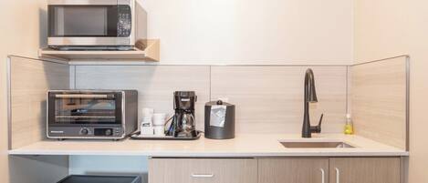 A compact kitchen with a microwave, toaster oven, coffee maker, and a sink.