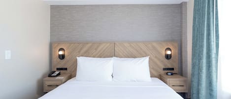 Una cama bien hecha con cabecera de madera, dos mesitas de noche con lámparas y vistas al exterior a través de una ventana con cortinas.