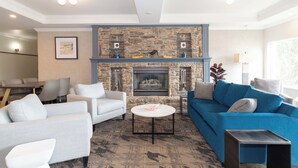 A modern living room with a stone fireplace, a blue sofa, and a white armchair. - Sandman Hotel Quesnel (Quesnel)