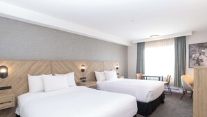A hotel room with two beds, a small table, a chair, and a desk. - Sandman Hotel Quesnel (Quesnel)